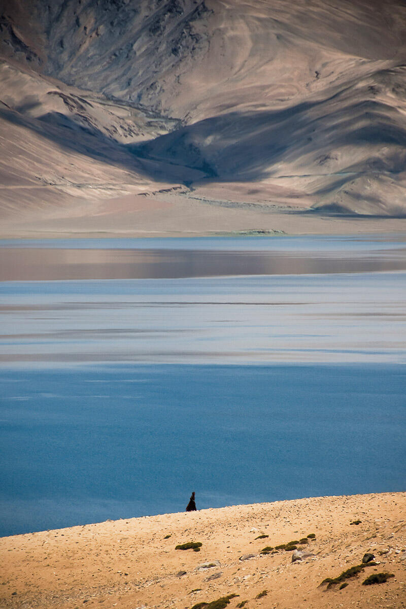 A nomad in traditional robe stands on the edge of Lake Tso Moriri in Ladakh, India