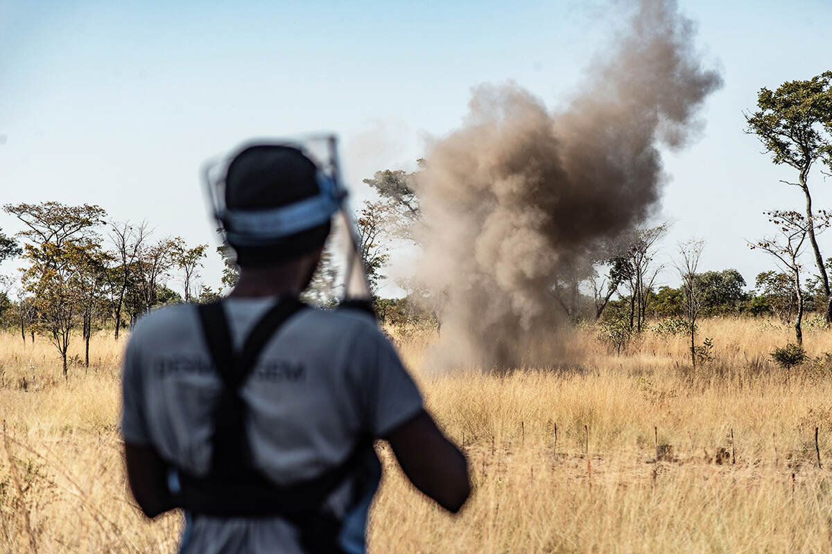 A man stands watching a controlled explosion of a landmine