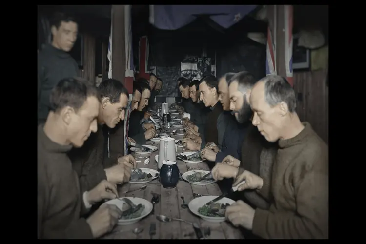 The ITAE crew members sit down for a Midwinter feast on the Endurance, five months after the ship became stuck in ice and four months before the crew was forced to evacuate