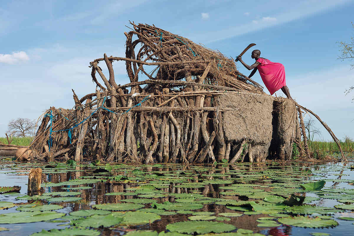 Nyachuana stands atop her home and demantles it surrounded by flood water