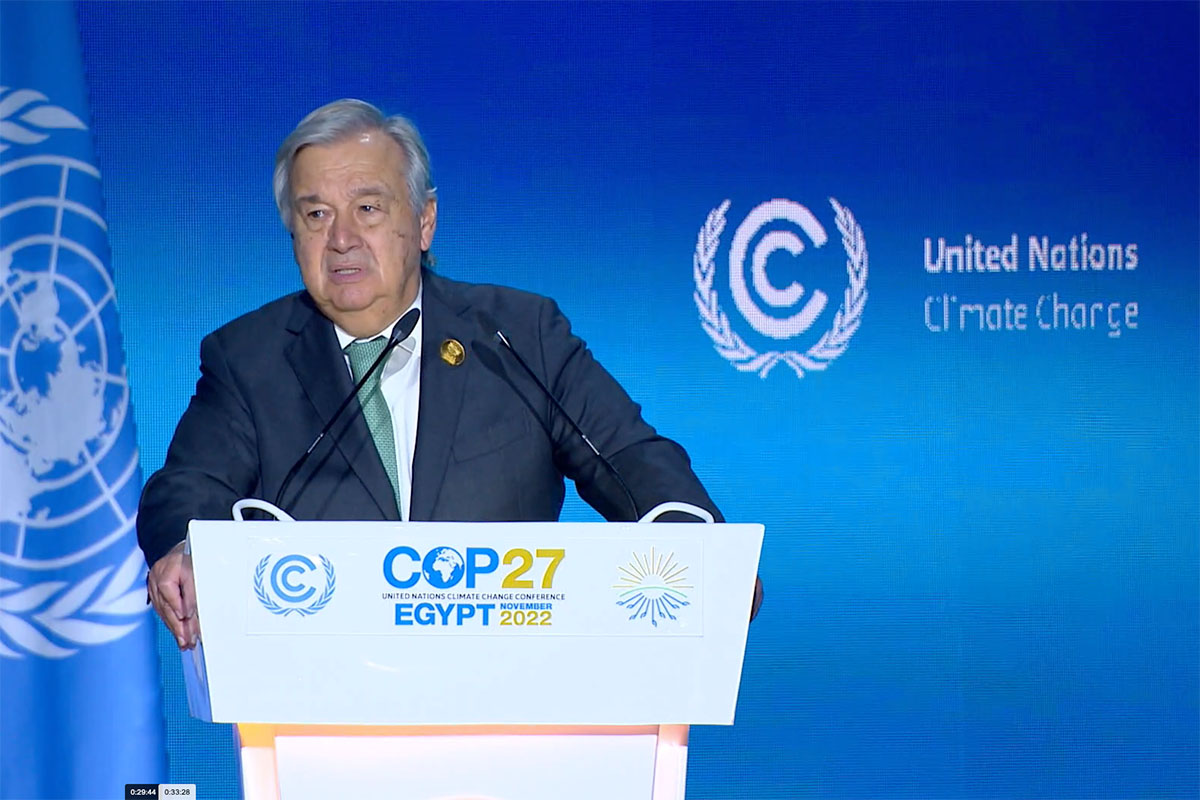 Guterres standing against a blue background behind a podium giving a speech