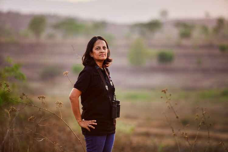 Krithi Karanth stands in a field wearing with binoculars around her neck