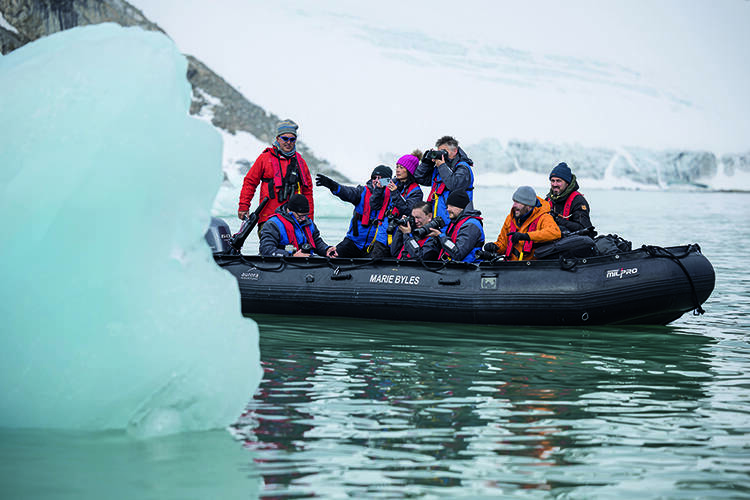 A group in a Zodiac take photos of a pale green iceberg