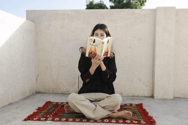 Shirin, Amina’s younger sister, 19, reads on the roof of her house. Shirin had plans to study psychology at university before the family was forced to leave.