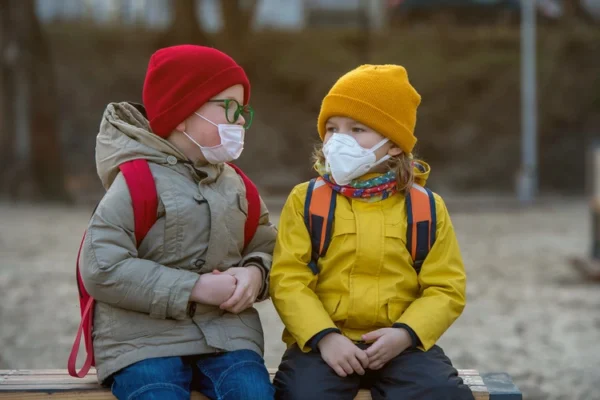 Child boy and girl playing outdoors with face mask protection.
