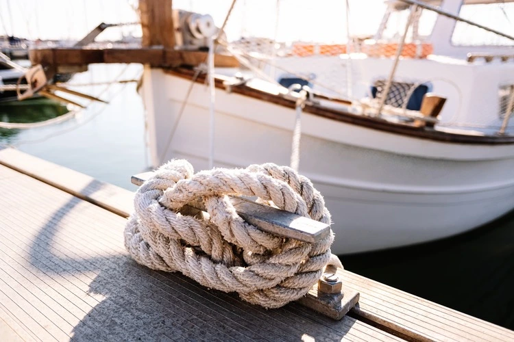 A close up of a fishing boat moored in a harbour, secured by an anchor and rope to a dock bollard.