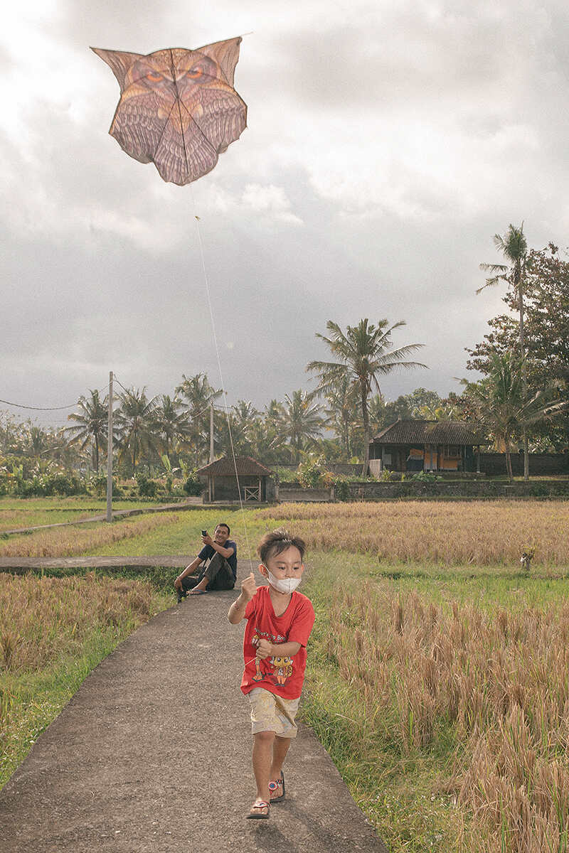 a boy runs down a path holding a kite with a man watching him