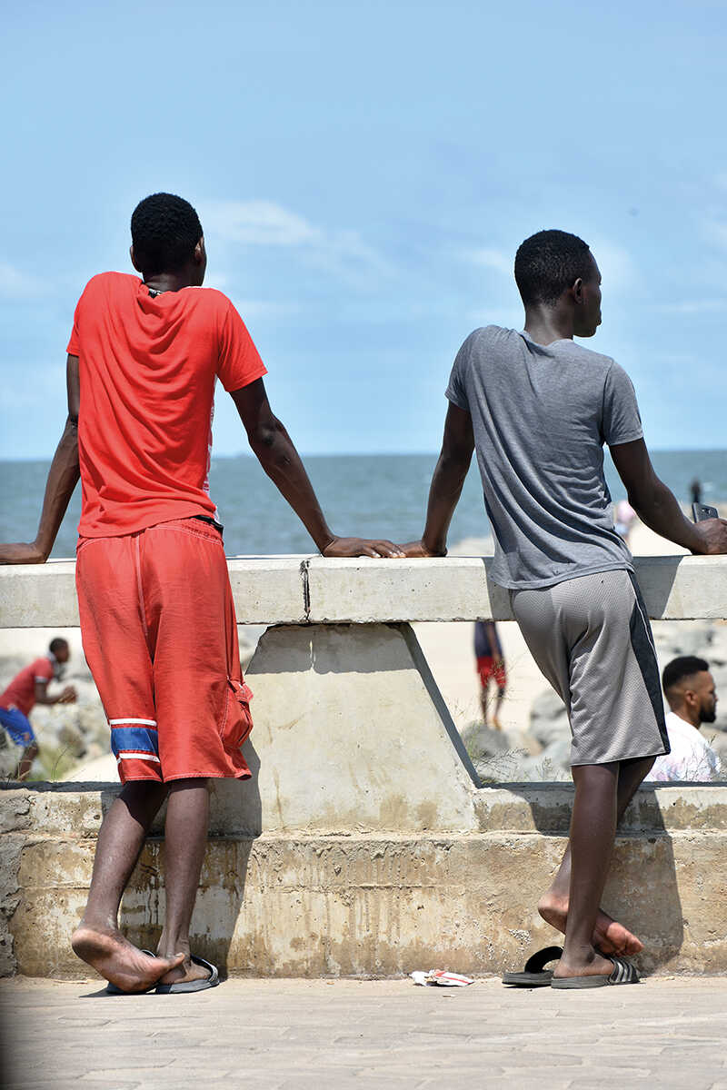 Two boys in orange and grey clothes look out over the water in madagascar