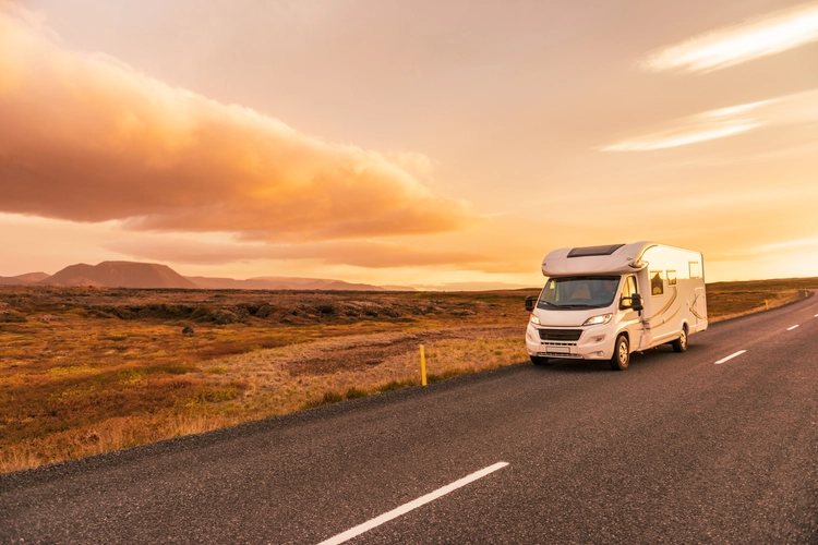 RV Motorhome camper van road trip. People on travel vacation adventure. Tourists in rental car campervan by view of mountains in beautiful nature landscape at sunset. From Iceland.