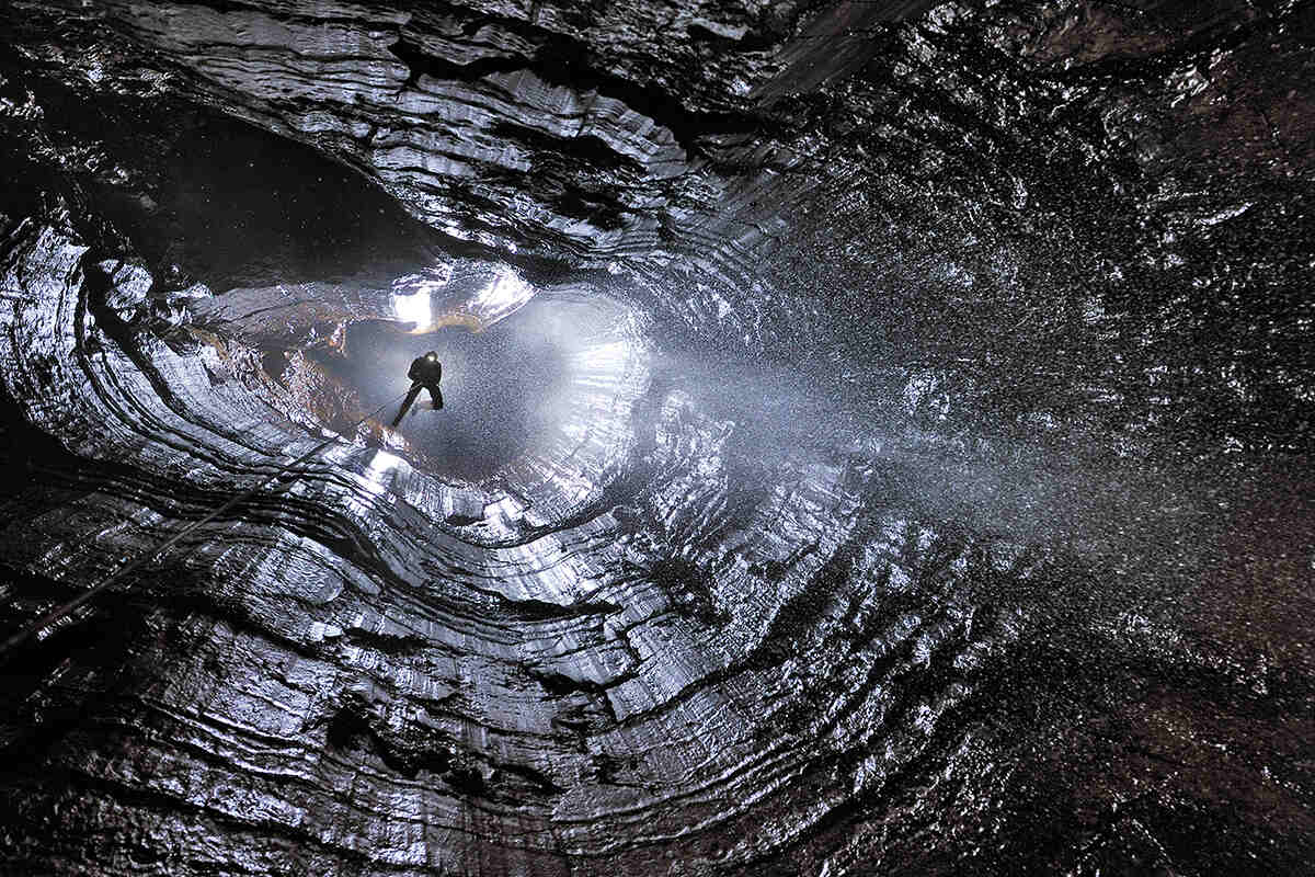 A person descends into a cave from above with water falling around them