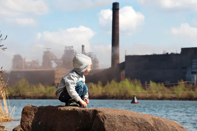 Playing little boy on the river coast in front of metallurgy plant