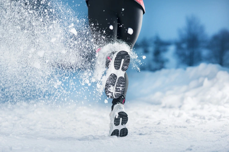 Woman athlete is running during winter training outside in cold snow weather.