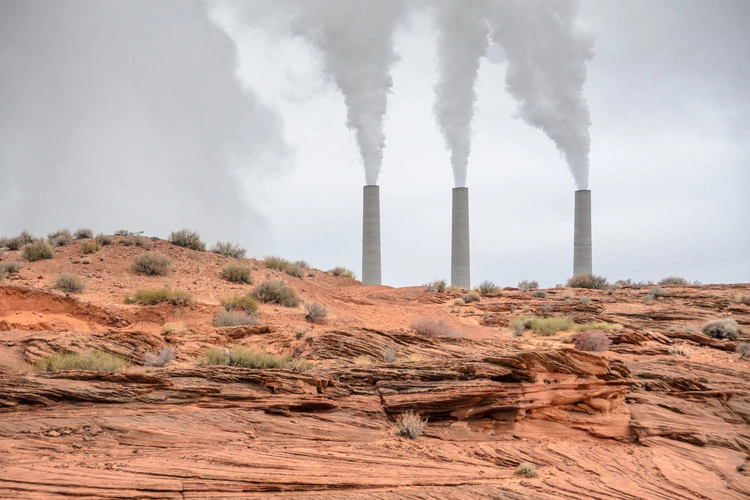 View of smoking smoke stacks of a generating station at the Navajo reservation, Arizona, USA. Desert landscape violated by an air polluting power plant, smog and gloomy sky. Polluting energy source.