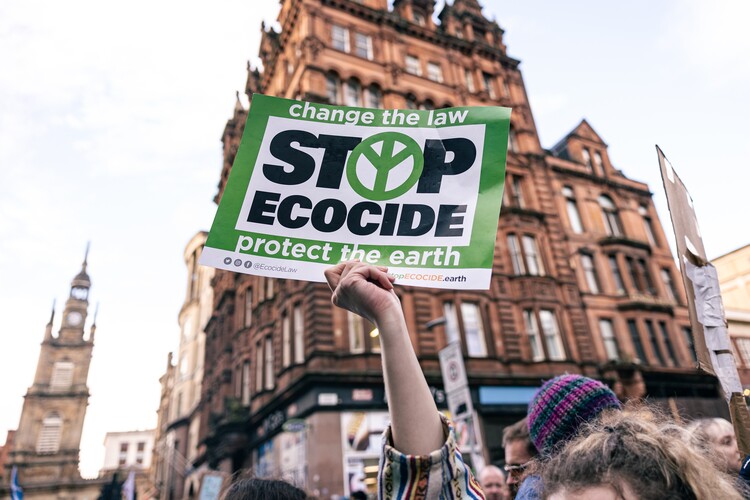 Selective focus shot of a protestor holding a sign saying "Stop Ecocide" at a climate protest in Glasgow, Scotland