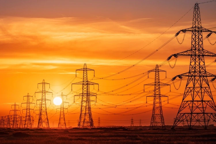 Sun setting behind the electric power lines running from Dungeness power station on the Kent coast south east England UK