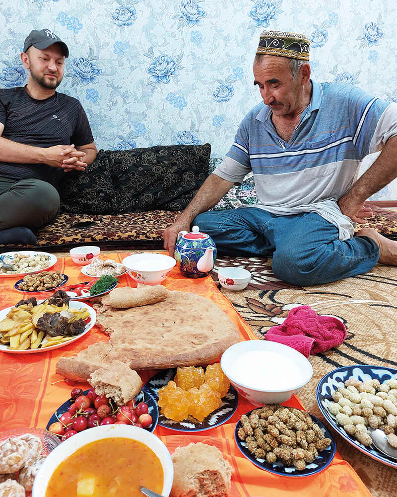 Two men sitting on rug having a feast