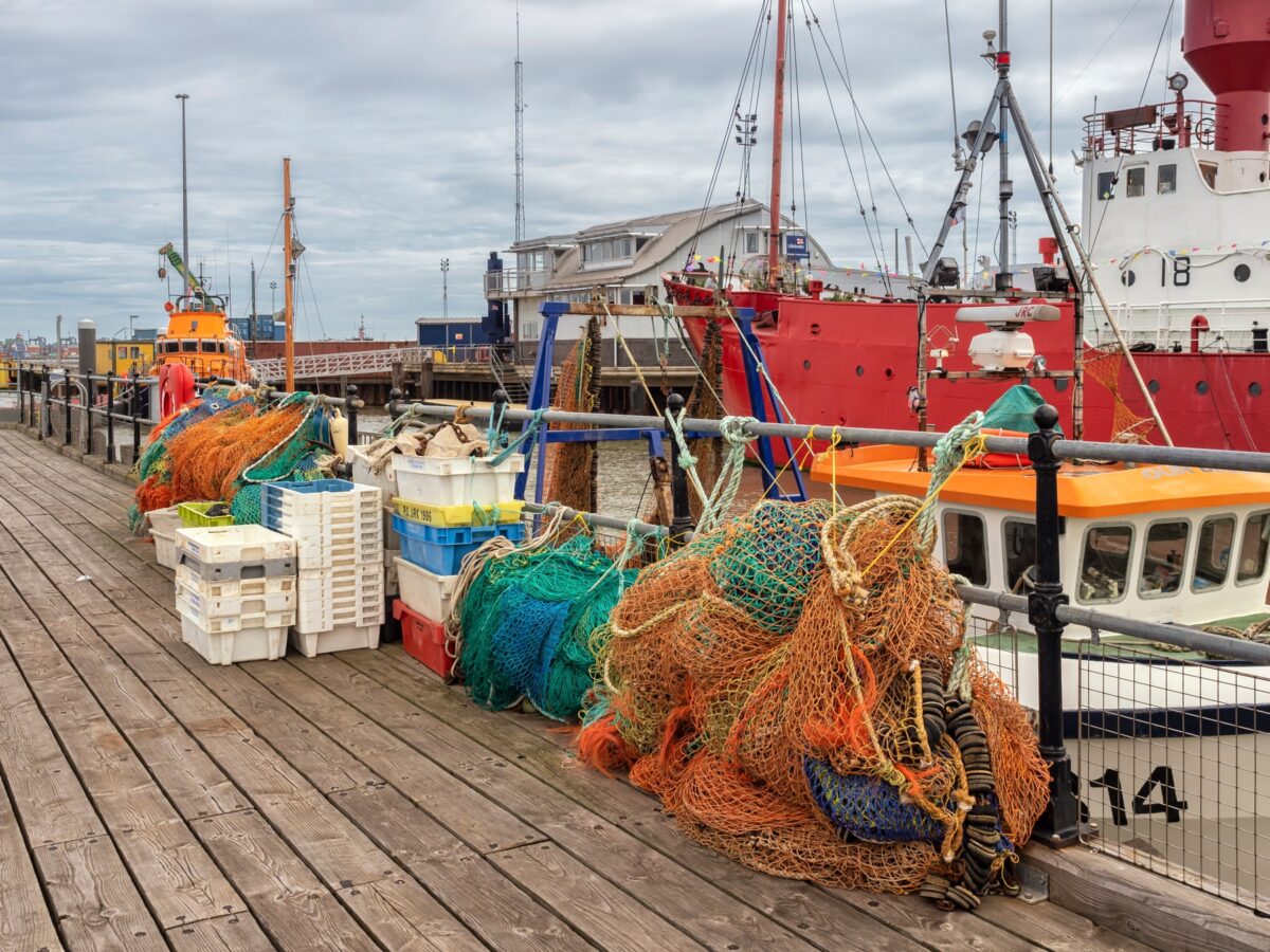 : View of the harbour with nets and crates on the quay with fishing trawlers in the background