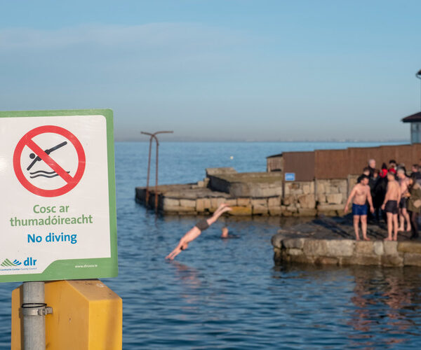 No diving sign with person diving in the background at Forty Foot during Christmas tradition. Dublin, Ireland. December 25, 2019