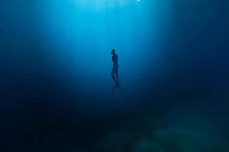 Freediver Swimming in Deep Sea With Sunrays. Young Man DIver Eploring Sea Life.
