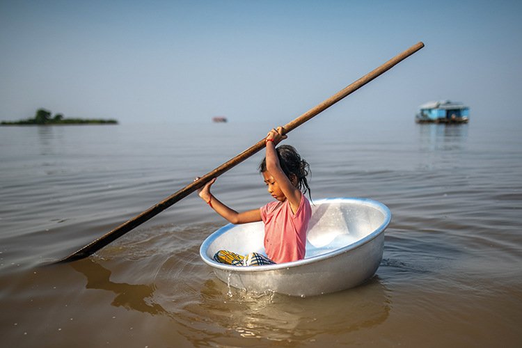 A girl paddles through the floating village of Oakol in a laundry bucket
