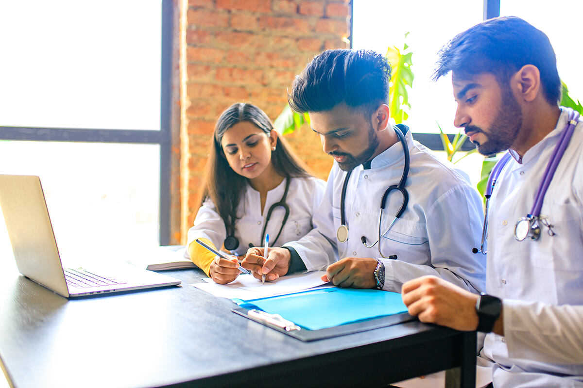 Three students sit at a desk studying medicine
