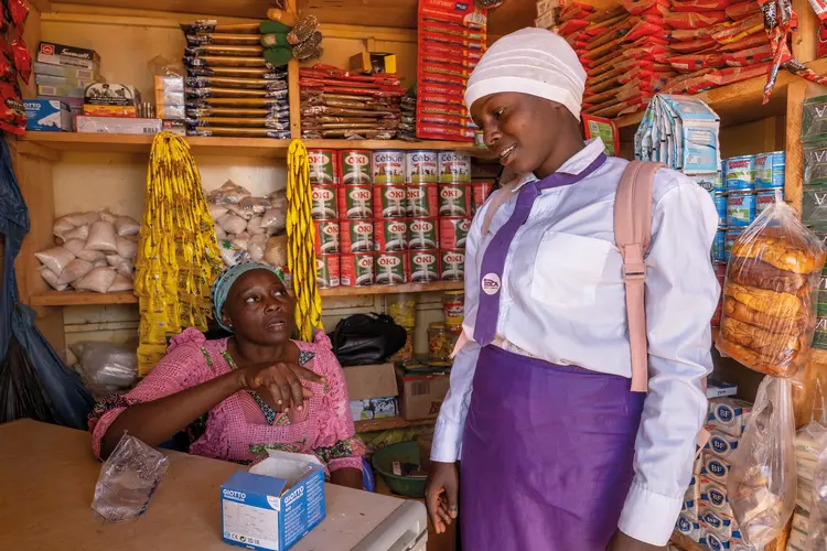 Kadi and her mother talking, with various food items on shelves behind them.