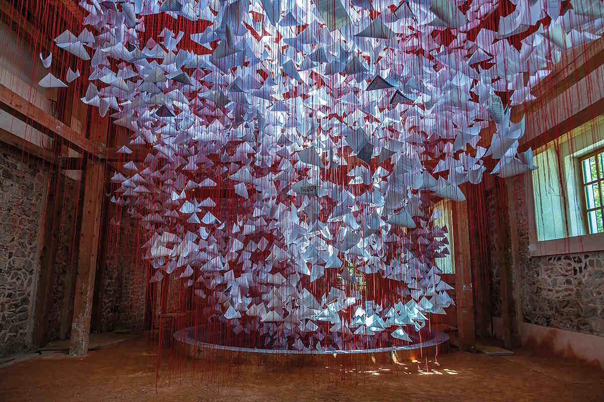 An art installation made of white paper and red thread hanging down in a room