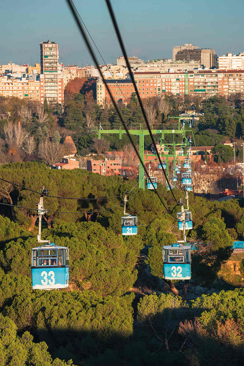 Blue cable cars soar over the trees and buildings of madrid