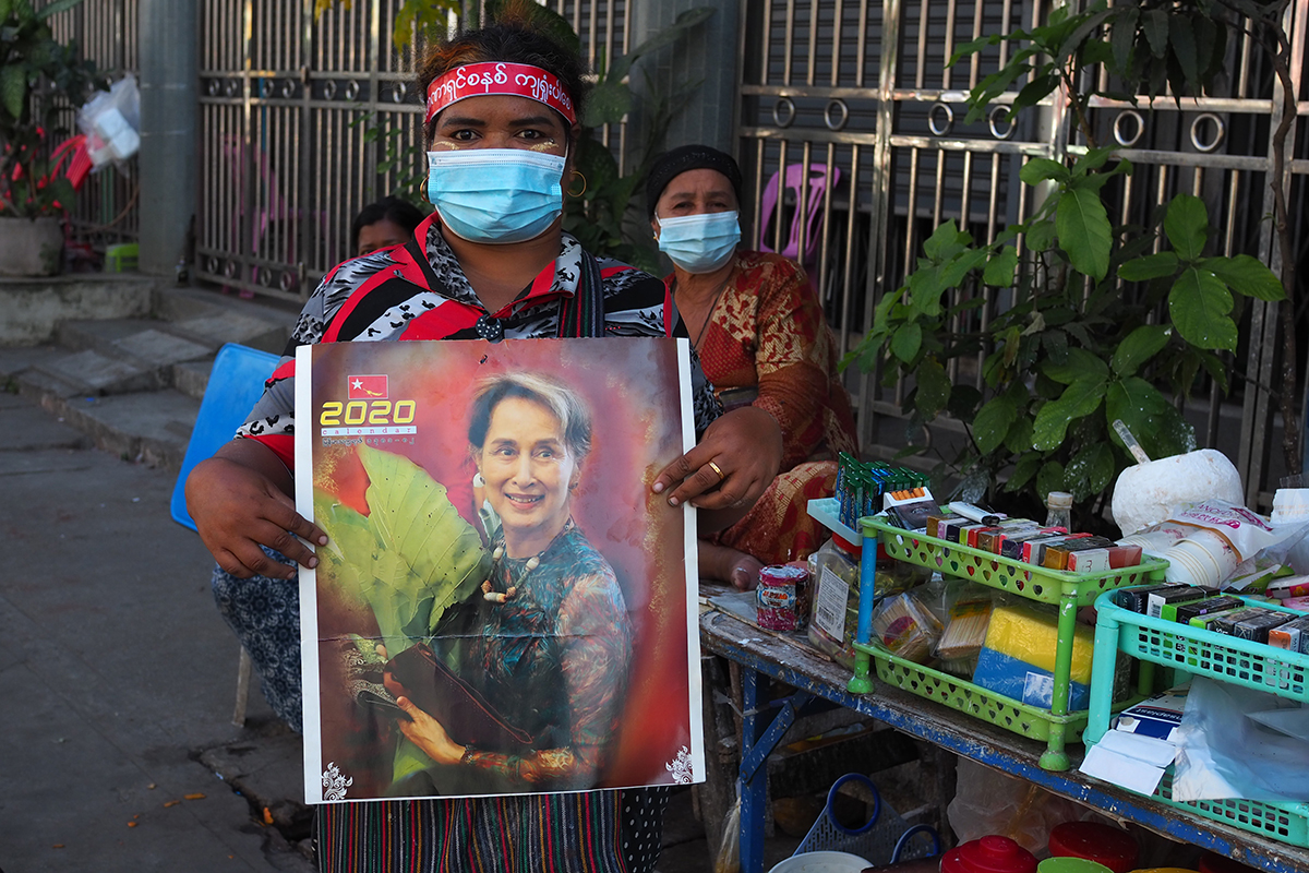 A woman protester in a street holding up a sign depicting Aung San Suu Kyi after her detention