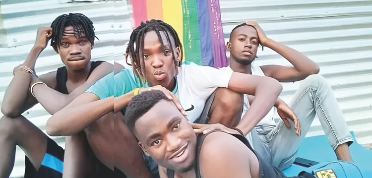 A group of young LGBTQ+ refugees sitting in front of a rainbow flag at Gorom