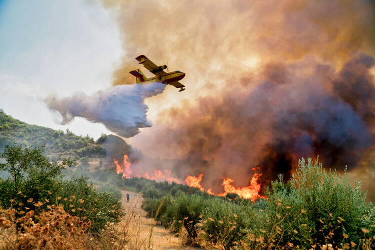 Peloponnese, Greece on 5 August 2021: A firefighting plane releases its load of water as it tries to extinguish a wildfire in Xelidoni village in the area of Ancient Olympia