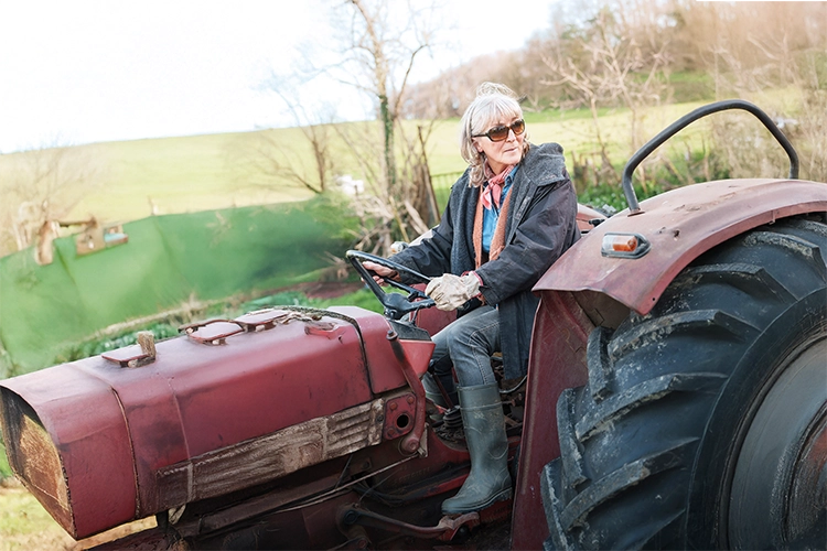 An elderly woman rides a tractor in the countryside