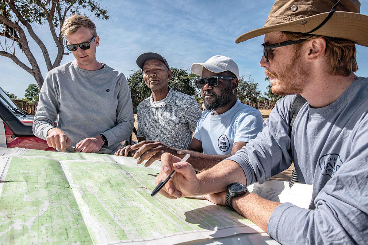 A group of men stand round a map showing minefield locations