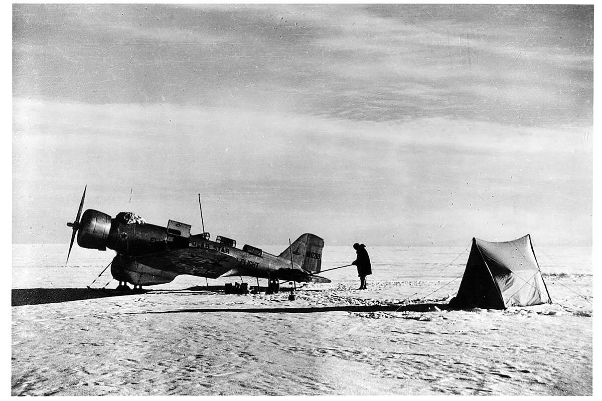 Black and white photo of a man working on a plane next to a tent snow on the ground