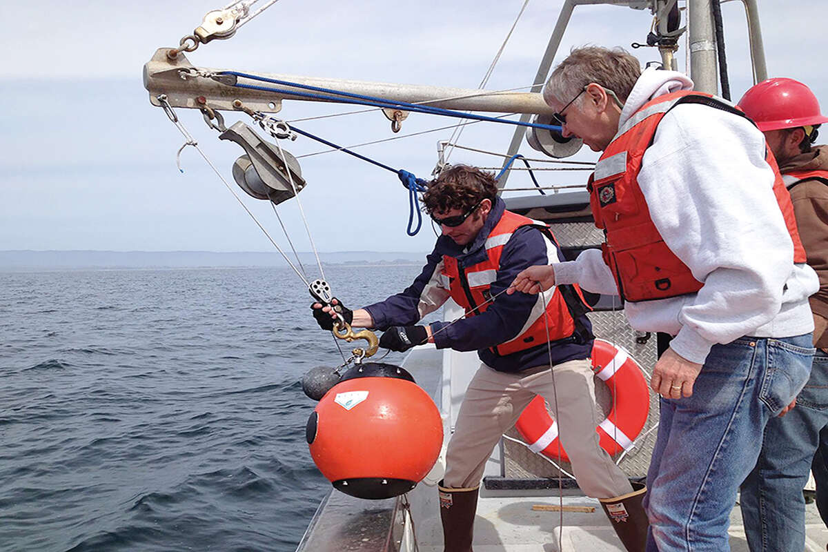 Two men on a boat on water prepare to launch a marine detector into the ocean