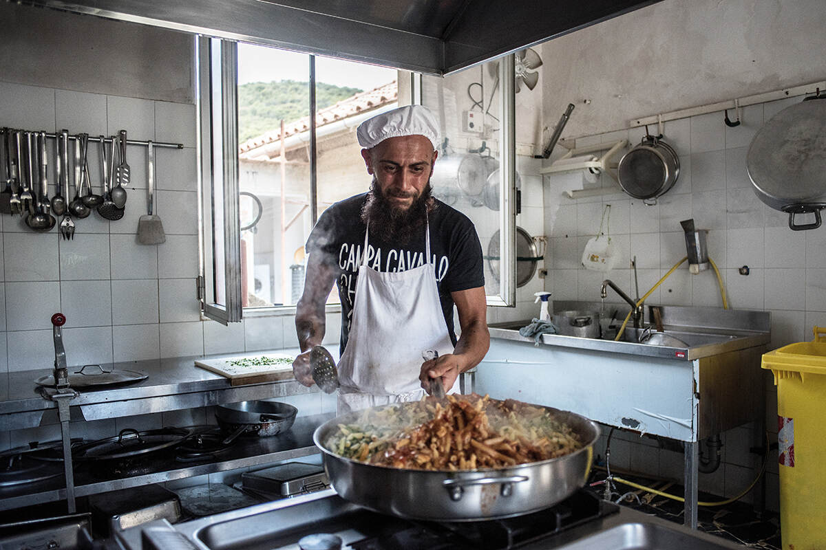 A man in chef uniform stands holding a pan with food in it in the prisons kitchen