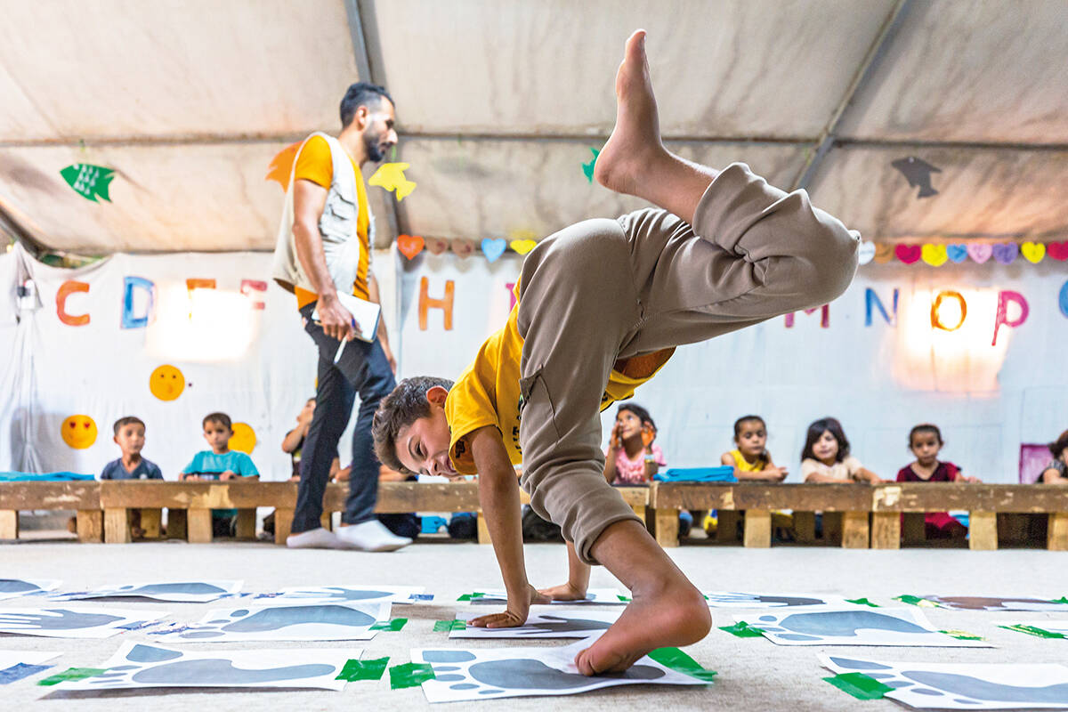 A child plays an acrobatic game as other children watch in a playtent at a refugee camp