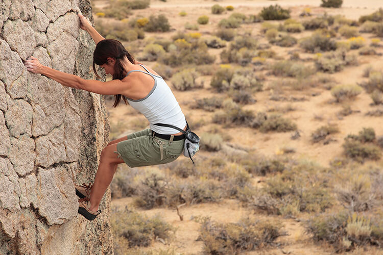 A woman climbs a rock face in the desert near Bishop, California