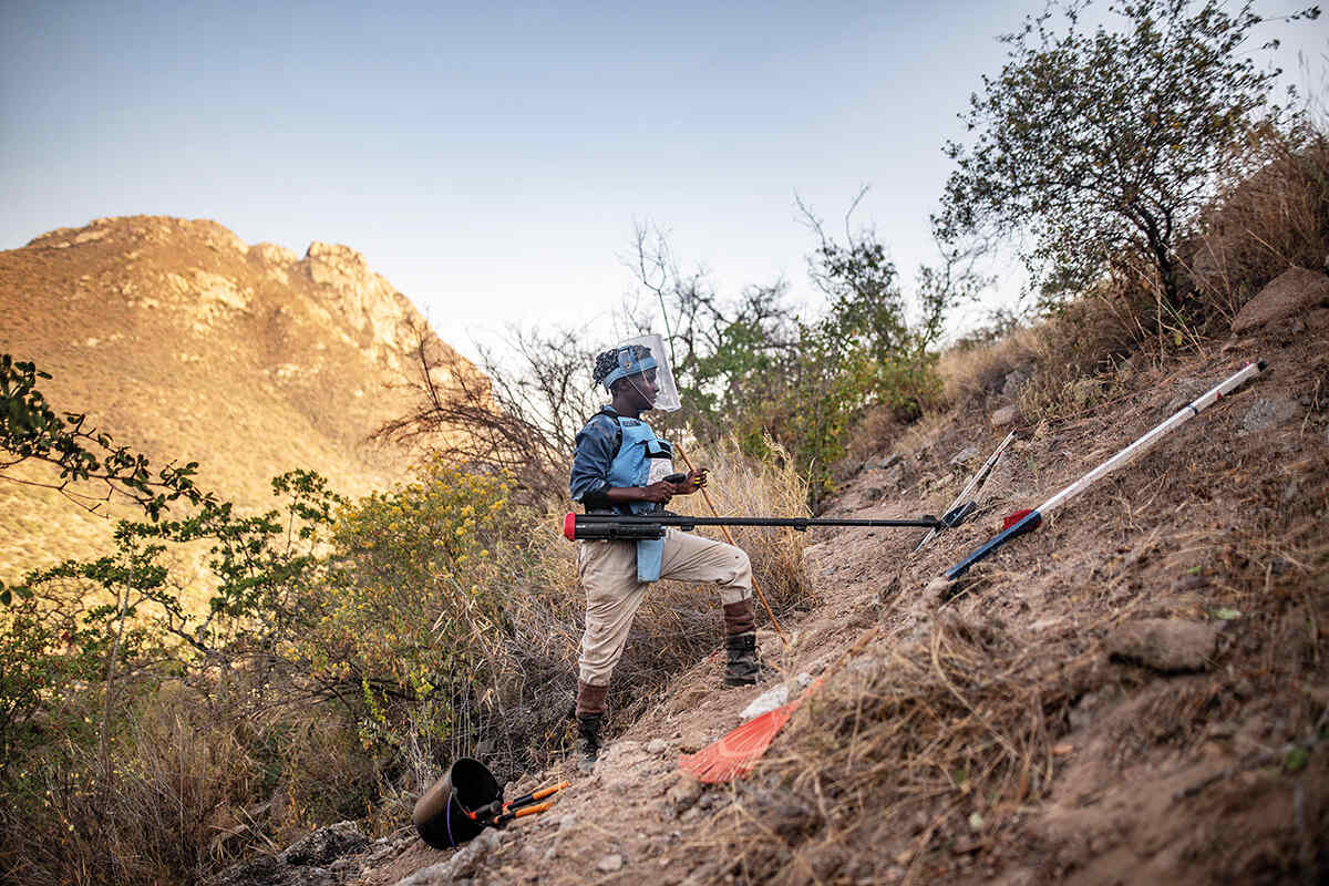 A woman scans for landmines on a steep rocky cliff