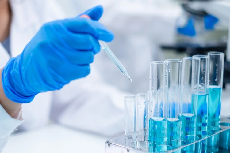 Close up of researcher dropping blue substance or liquid into test tube