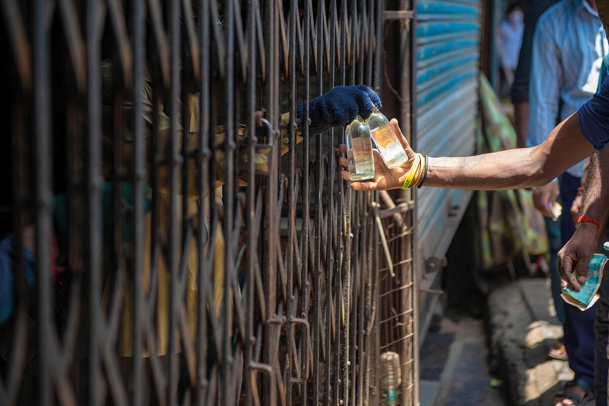 A person hands a man some illegal alcohol through a shop fence