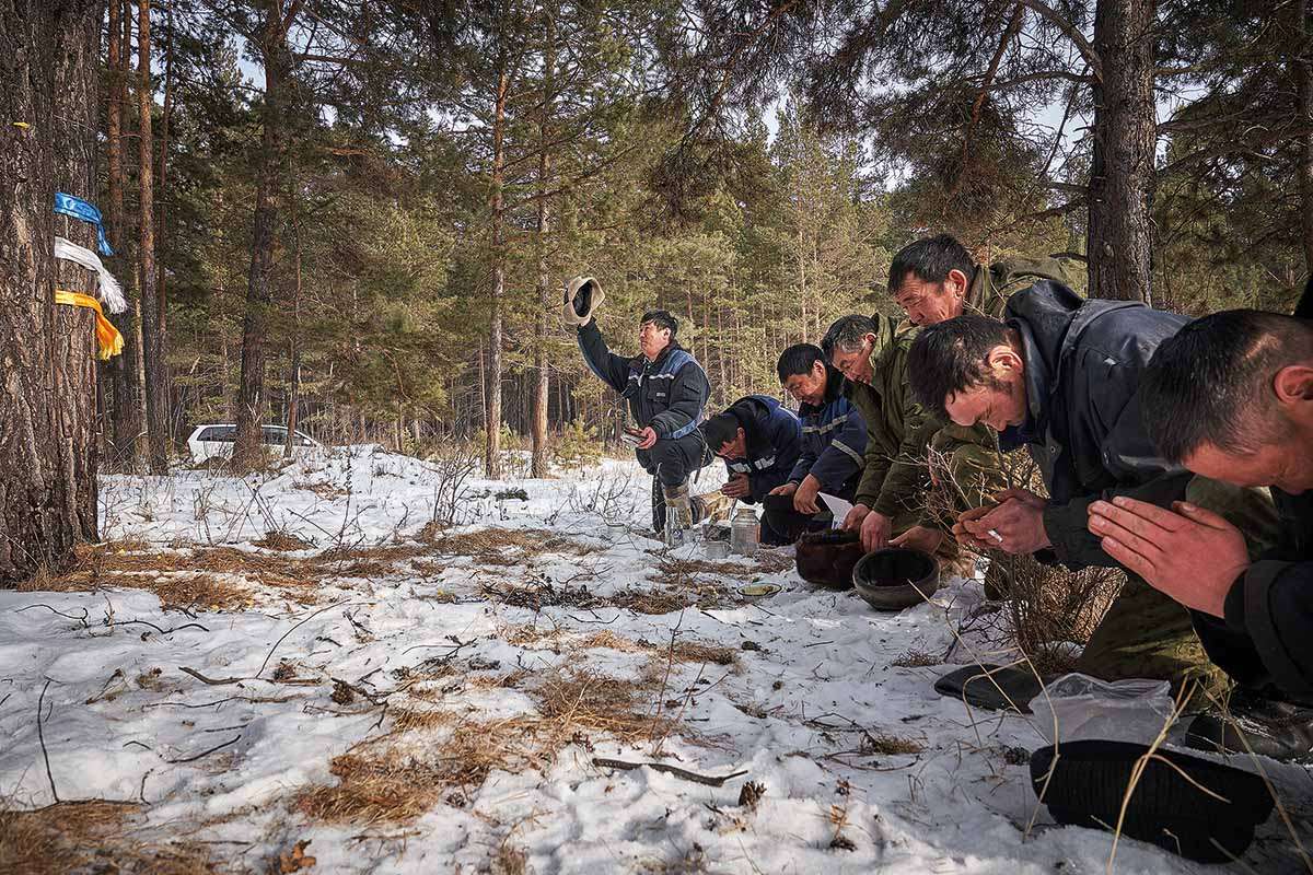 Men pray before a tree wrapped in colour ribbons