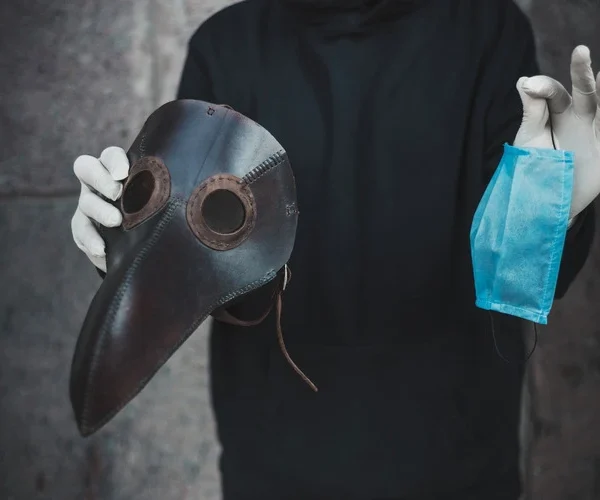 Man holds a mask of plague doctor and disposable medical mask.