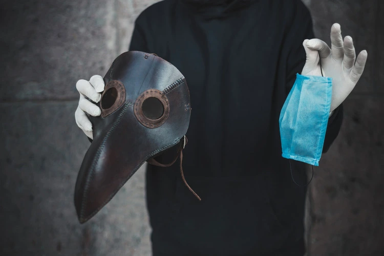 Man holds a mask of plague doctor and disposable medical mask.