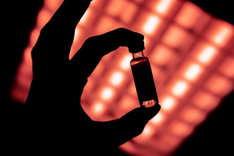 vaccine vial held against red light, showing its black silhouette,