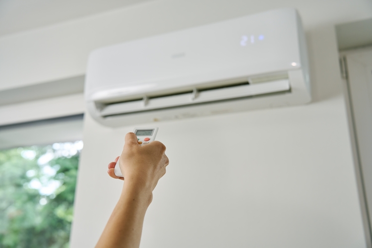 Adjusting air conditioner temperature with remote control. Hand holds remote control and setting