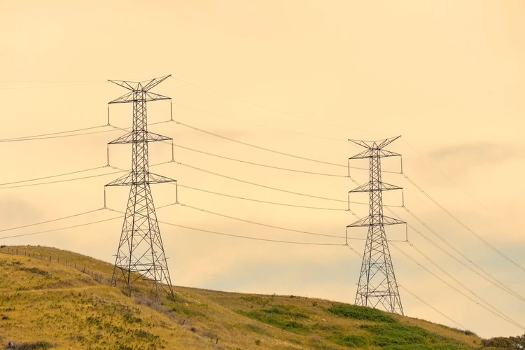 Photograph of a large electricity Transmission Tower on a grassy hill against an orange sunset sky in regional Australia.