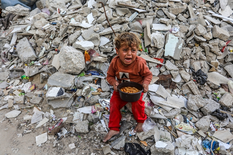 Child with food, next to rubble