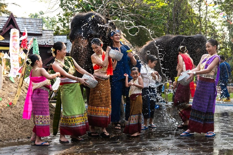 Group of man, women and children in traditional Thai costumes having fun splashing water to each other on Song kran festival in elephant camp, Chiangmai Thailand