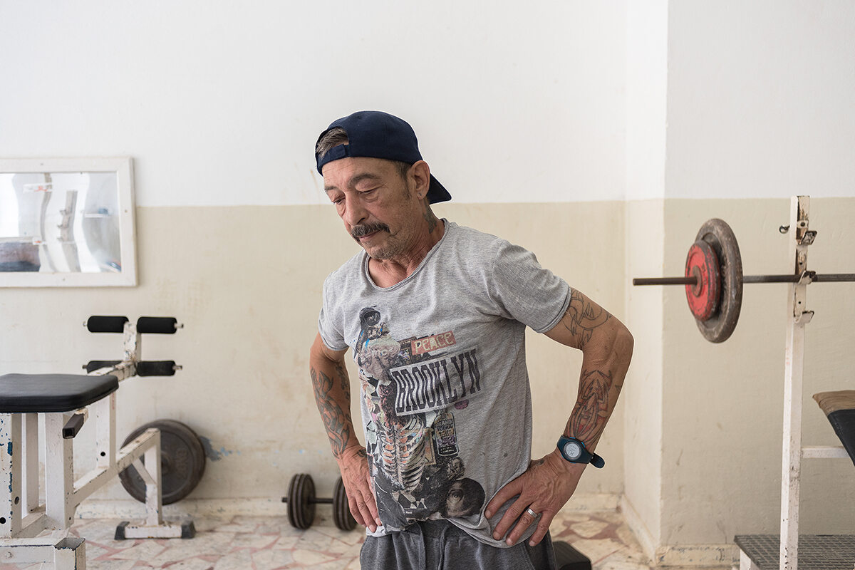 A man with tattoos stands in the prison gym with gym equipment in the background